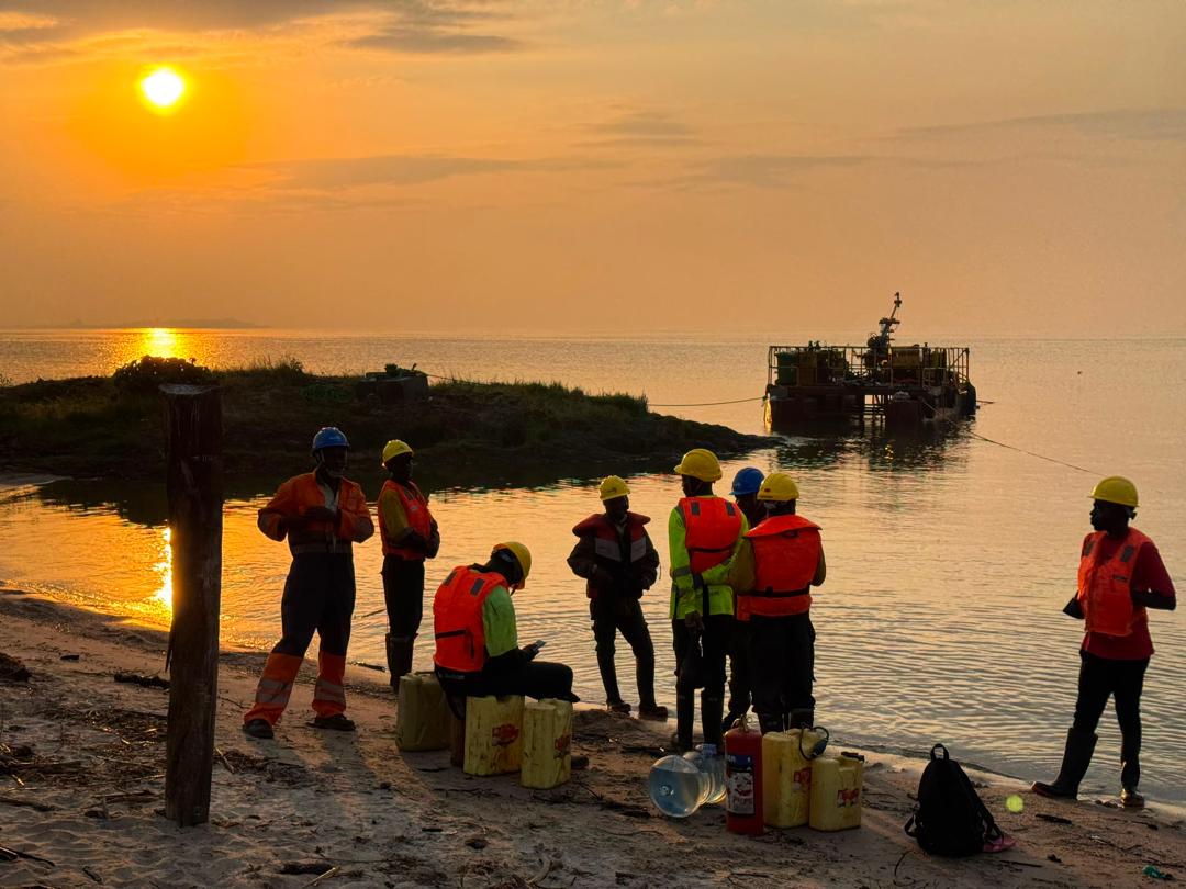 Tectoni crew on the shoreline at sunset with a drilling barge offshore