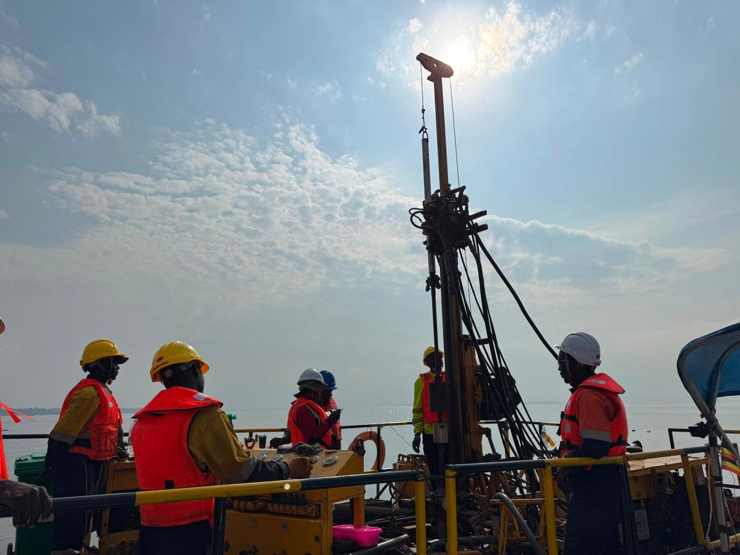 Crew in life vests operating a drill rig on a barge under a bright sky