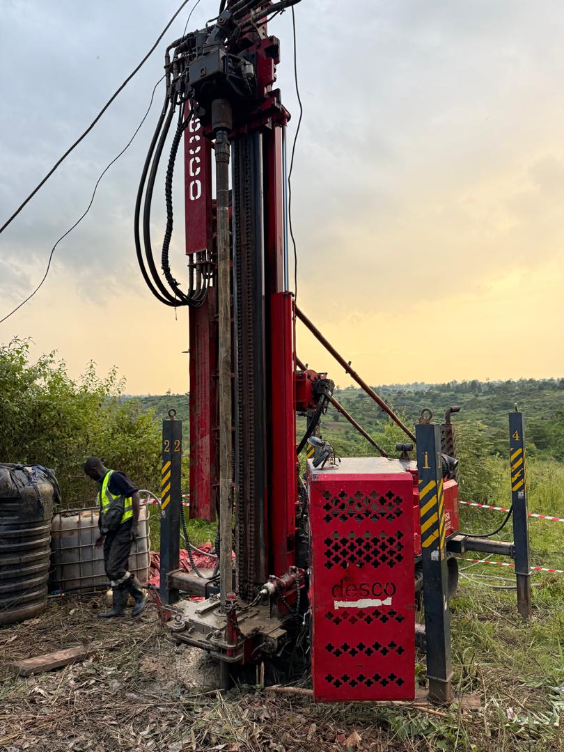 A red core-drilling rig standing against a warm evening sky